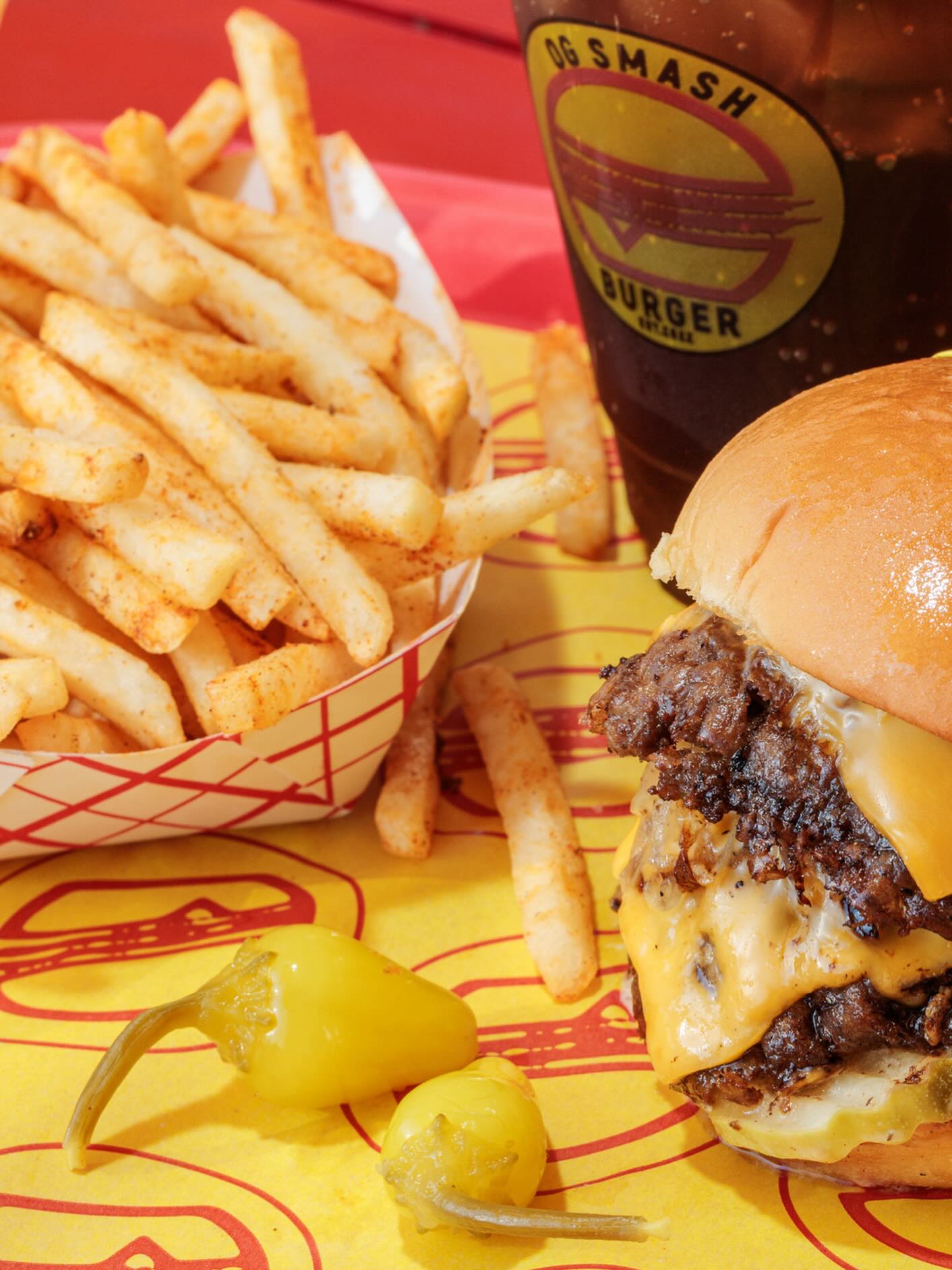 OG Smash Burger combo: smash burger with cheese, golden fries, pepperoncini and iced drink on yellow branded paper